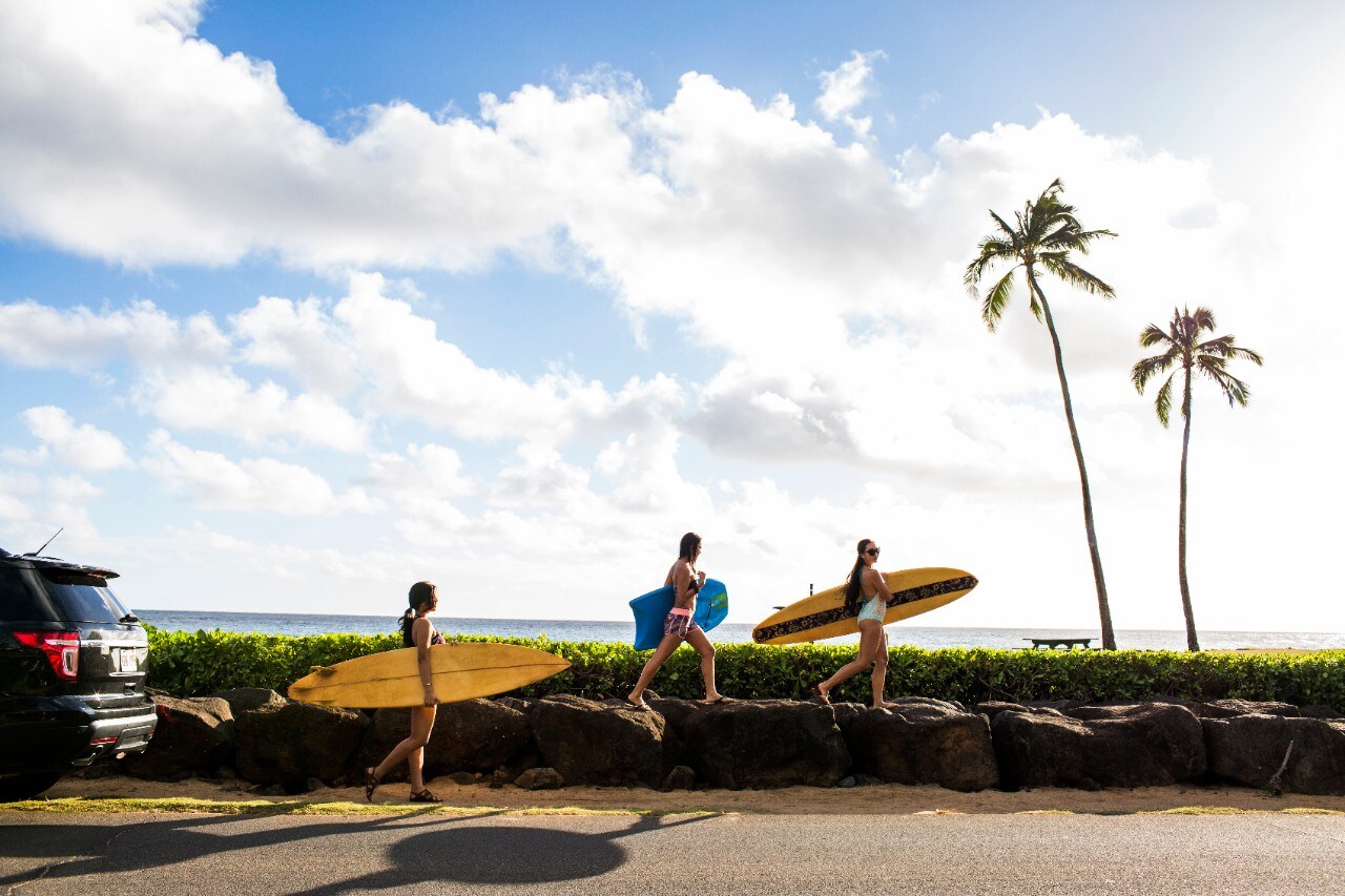 Pacific Islander surfers carrying surfboards on rock wall